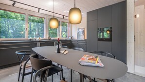 Cozinha moderna com mesa de jantar, cadeiras, luminárias pendentes e vista para o verde lá fora.