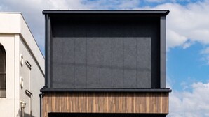 A modern building with a flat roof, a large entrance, and a small garden area with plants and a stone wall. - nagisa awajishima (Awaji)