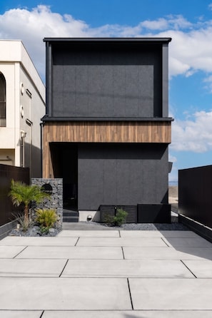 Un edificio moderno con techo plano, una entrada amplia y un pequeño jardín con plantas y un muro de piedra.