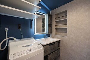 A modern bathroom with a built-in washer and dryer, a large mirror, and a shelf unit.