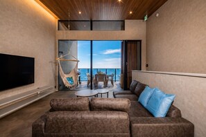 A modern living room with a large flat-screen TV, a brown leather sofa, a hanging chair, and a balcony with a view of the sea. - nagisa awajishima (Awaji)