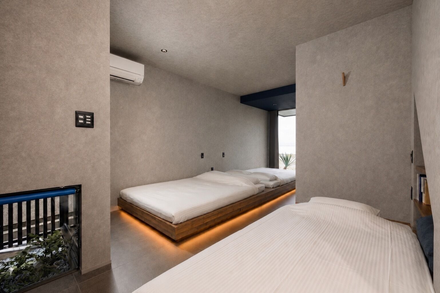 A modern bedroom with a central bed, a small bedside table, and a window with a view.
