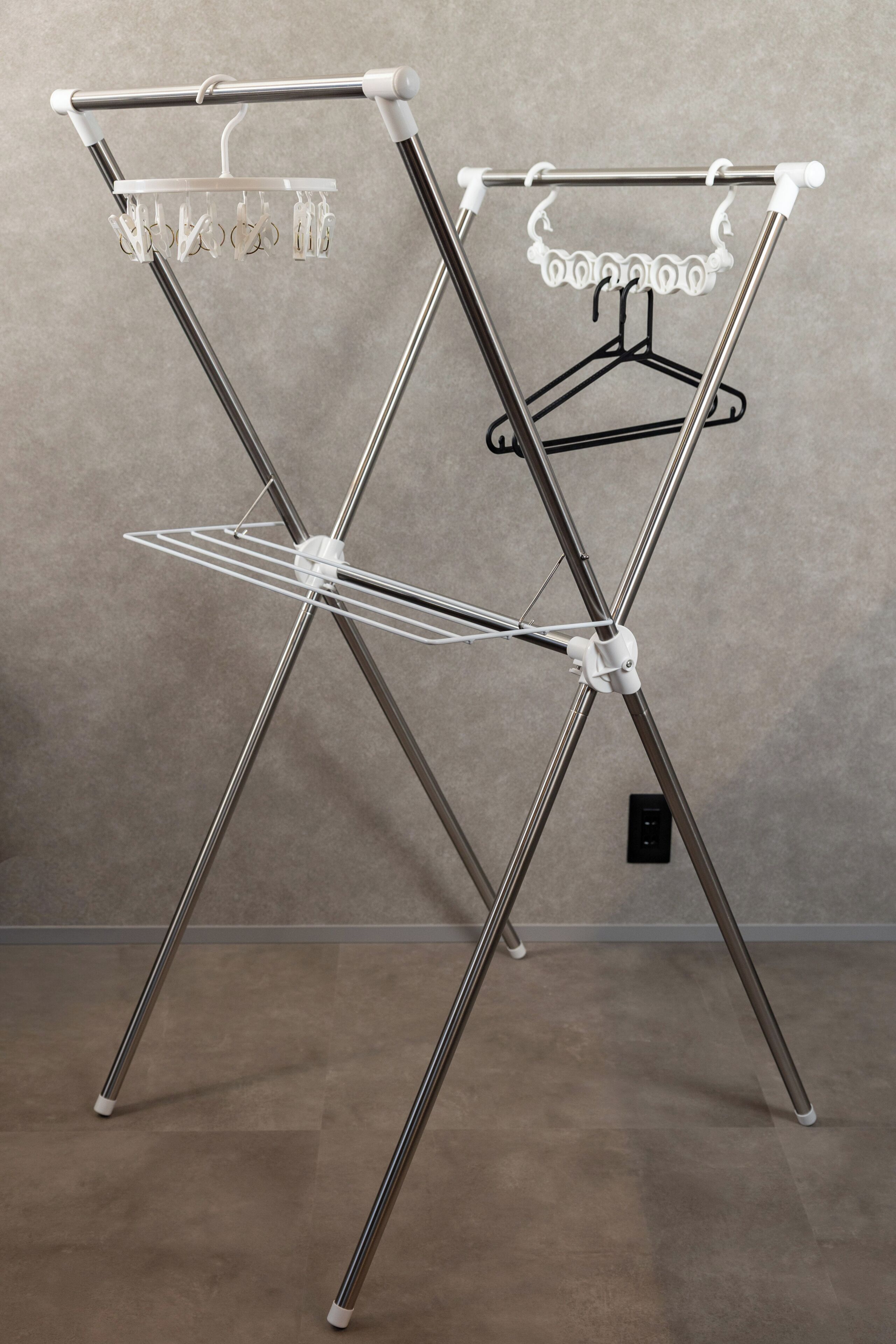 A metal drying rack with a hanger and a wire rack, set against a plain wall.