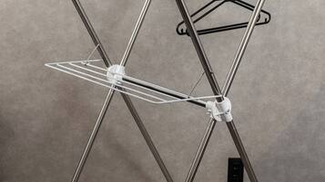 A metal drying rack with a hanger and a wire rack, set against a plain wall.