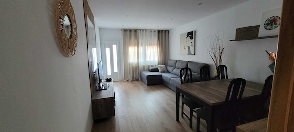 Una sala de estar con un sofá, una mesa de comedor con sillas, un televisor y un espejo.