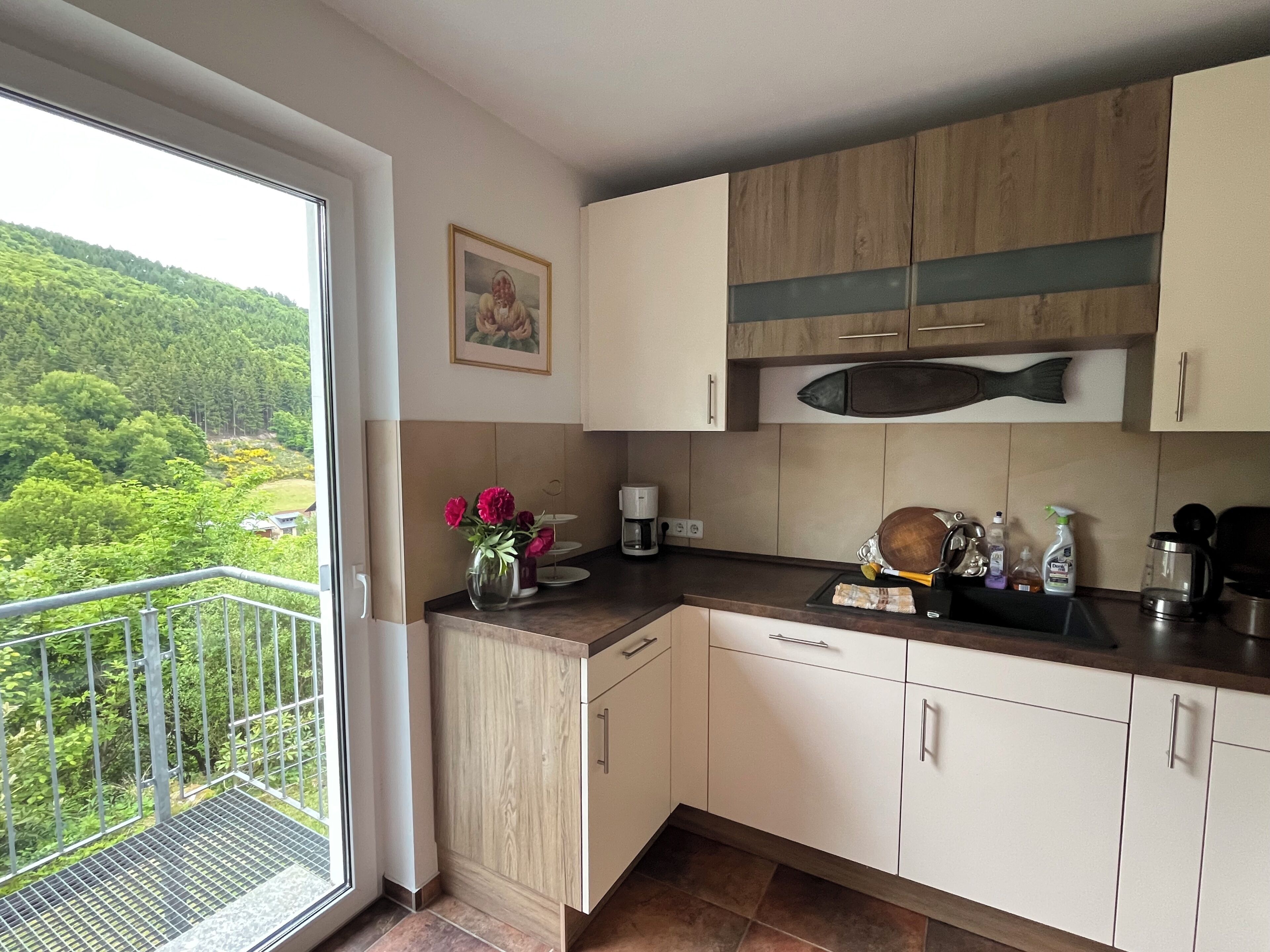 Uma cozinha moderna com vista para uma paisagem verde, armários de madeira e um pequeno vaso com flores.