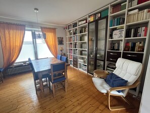 A room with a wooden floor, a dining table with chairs, a white armchair, and a bookshelf filled with books. - Quietly located vacation apartment (Medebach)