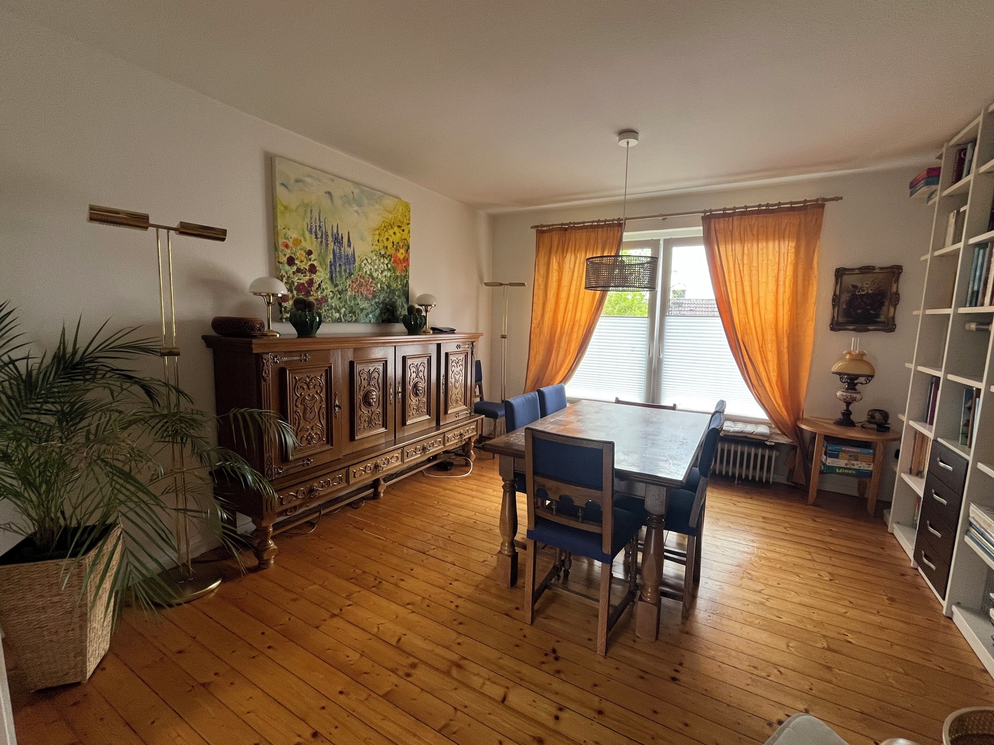 A dining area with a wooden table and chairs, a cabinet with decorative items, and a painting on the wall.