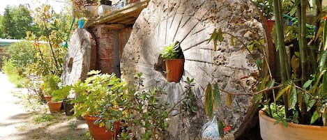 A rustic outdoor setting with potted plants, a large decorative wheel, and a lantern.