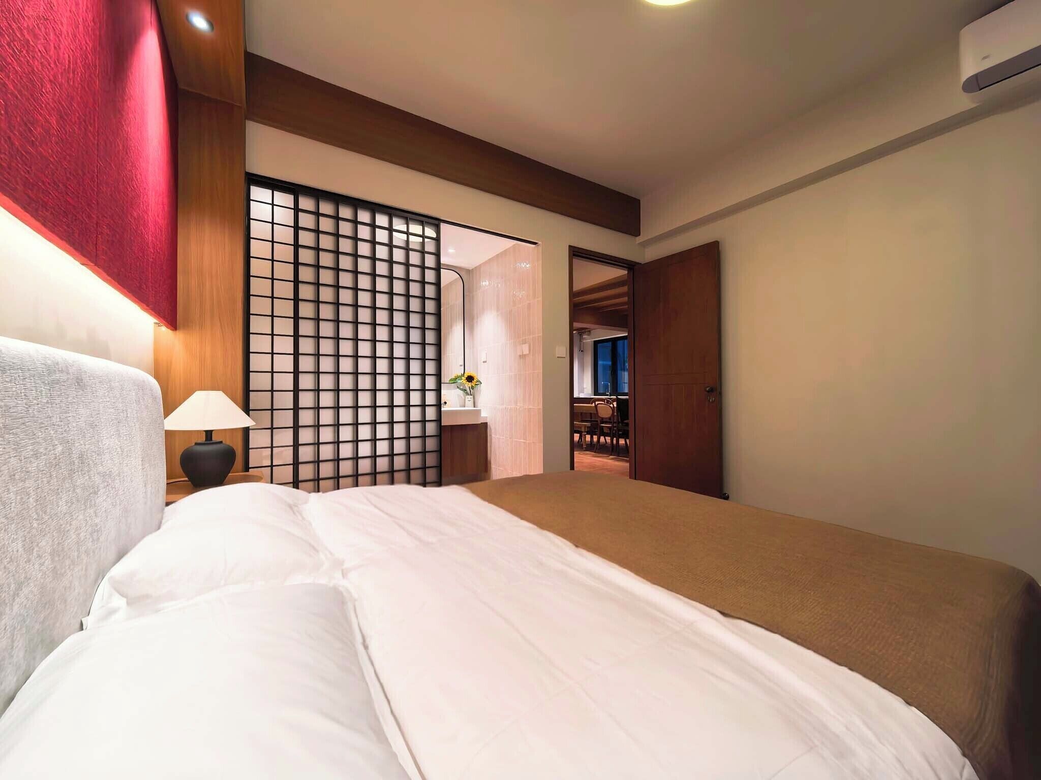 Quarto de hotel com cama, mesa de cabeceira, abajur, televisão fixada na parede e porta deslizante para um banheiro.
