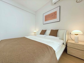 Una cama bien hecha con una manta marrón, almohadas blancas y un cuadro colgado en la pared.