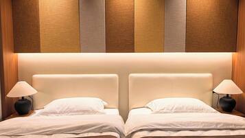 Habitación de hotel con dos camas, cada una con cabecera, lámparas de noche y una decoración en tonos neutros.