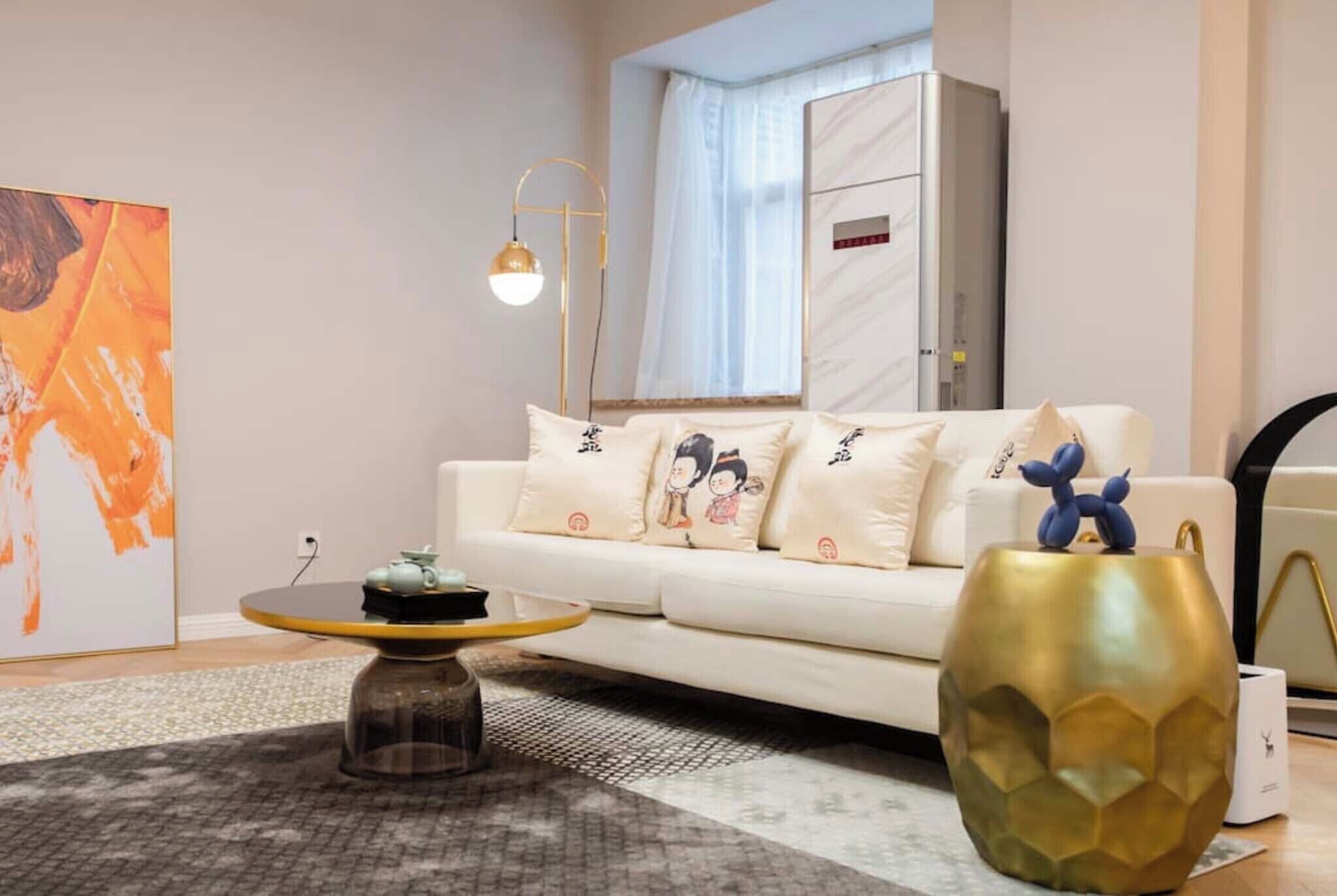 Uma sala de estar moderna com um sofá branco, almofadas decorativas, uma mesa de centro redonda e um vaso dourado grande.