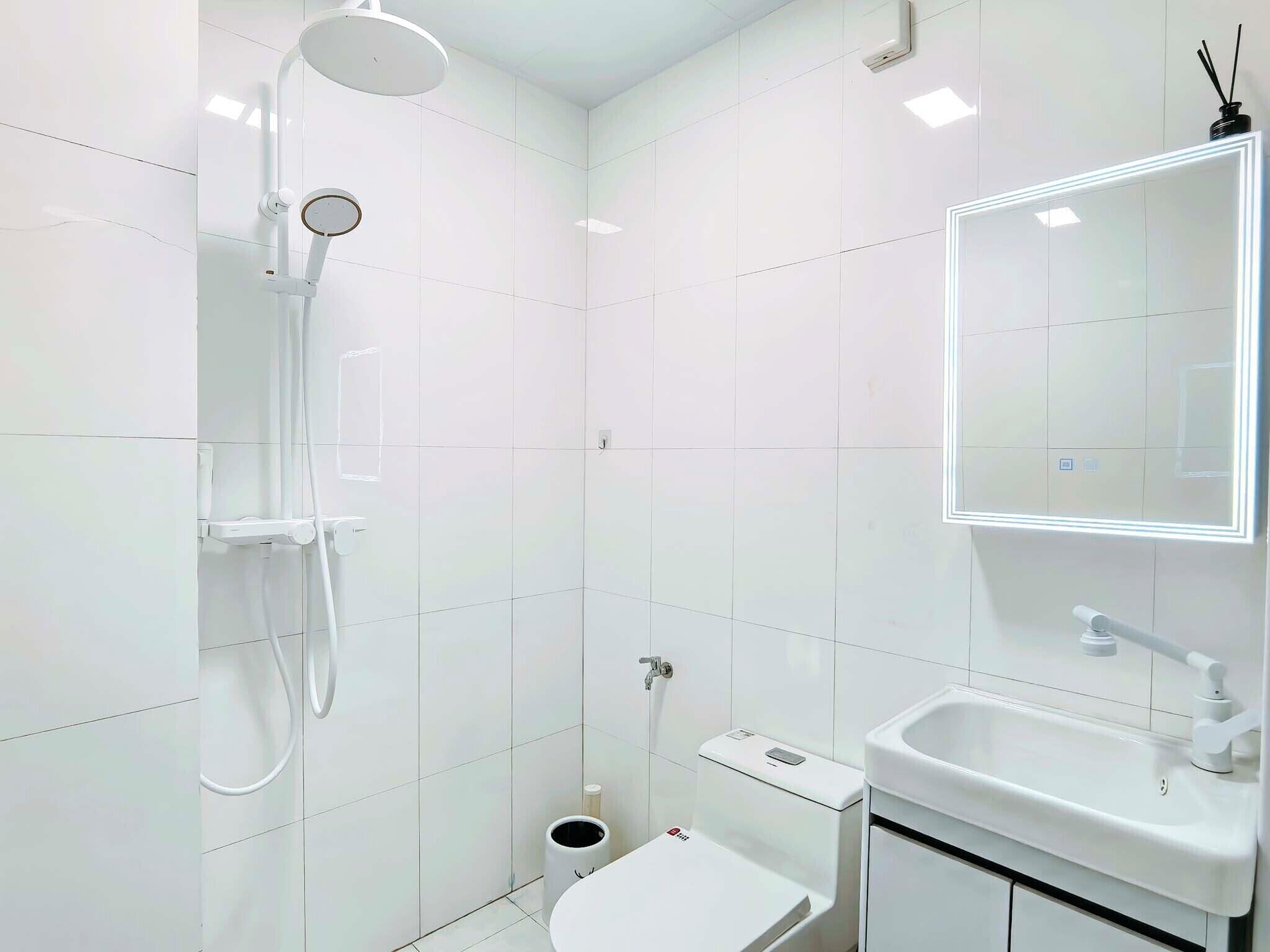 A modern bathroom with white tiles, a shower, a sink, and a toilet.