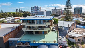 A multi-story hotel with a rooftop pool, surrounded by other buildings. - Hamptons on Wharf - Beautifully appointed apartment in the centre of Forster with stunning lake view (Forster)