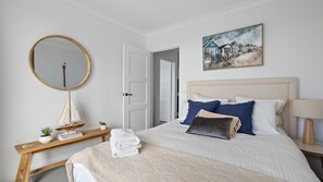 A bedroom with a bed, a bedside table, a mirror, a painting, and a door. - Hamptons on Wharf - Beautifully appointed apartment in the centre of Forster with stunning lake view (Forster)