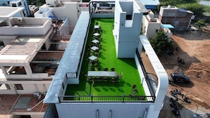 A rooftop terrace with a green artificial lawn, outdoor seating, and a view of surrounding buildings. - 3-bedroom Premium Serviced Apt right in front of Vaigai River, Kochadai, Madurai (Madurai)