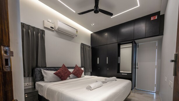 A modern hotel room with a bed, a ceiling fan, an air conditioning unit, a wardrobe, and a door. - 3-bedroom Premium Serviced Apt right in front of Vaigai River, Kochadai, Madurai (Madurai)