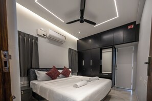 A modern hotel room with a bed, a ceiling fan, an air conditioning unit, a wardrobe, and a door. - 3-bedroom Premium Serviced Apt right in front of Vaigai River, Kochadai, Madurai (Madurai)