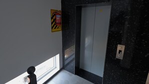 A modern elevator with a digital display, a fire extinguisher, and a window providing natural light. - 3-bedroom Premium Serviced Apt right in front of Vaigai River, Kochadai, Madurai (Madurai)