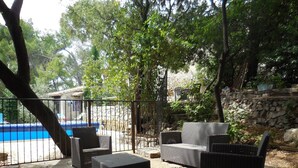Eine Terrasse im Freien mit Korbmöbeln, einer Steinmauer und einem Pool im Hintergrund.