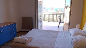 Une chambre avec un lit, une commode bleue, un radiateur et un balcon avec vue.