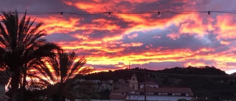 A sunset with a vibrant sky, palm trees, a swimming pool, and a building in the background.