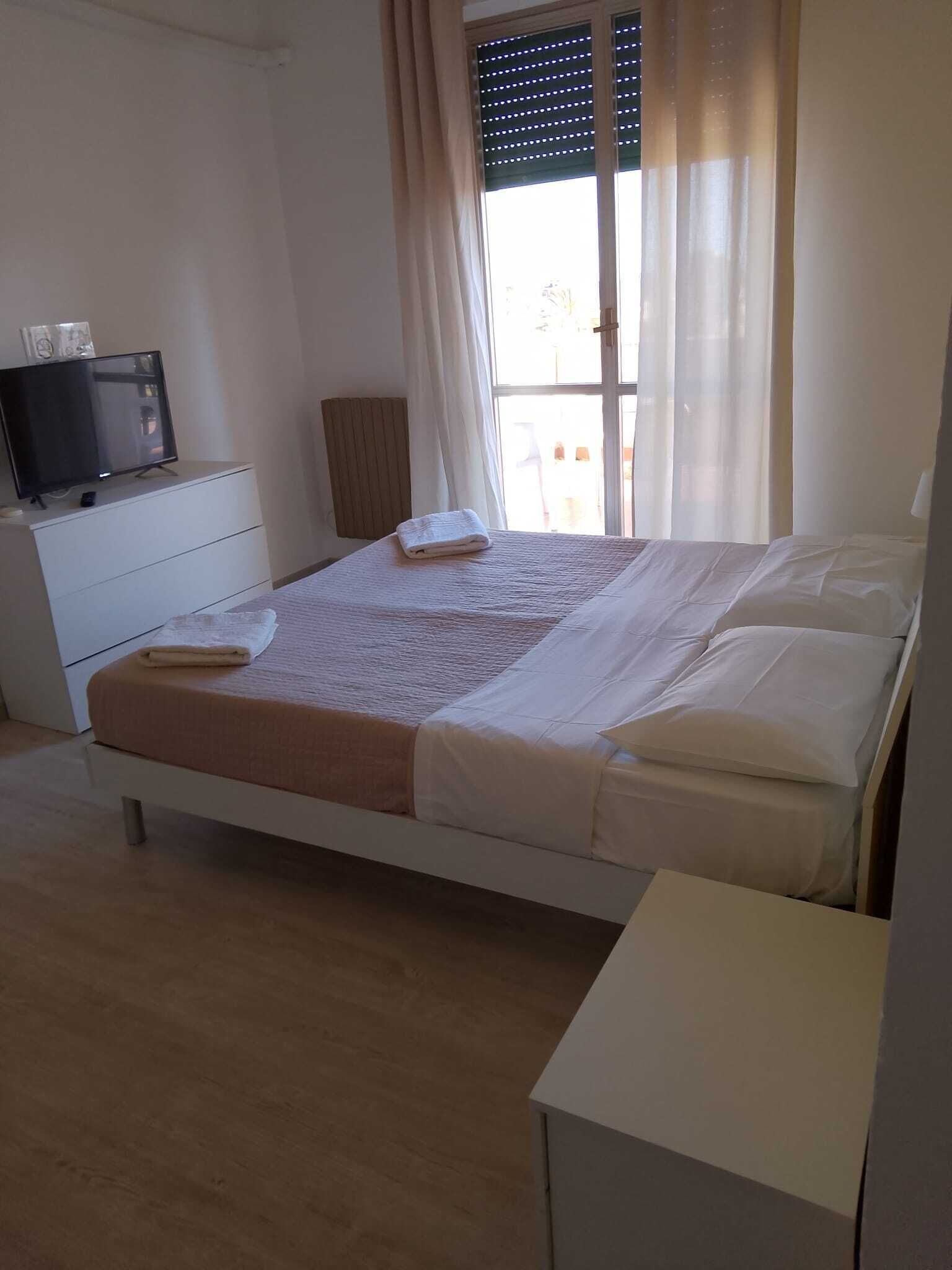 A bedroom with a bed, a TV on a dresser, and a window with curtains.