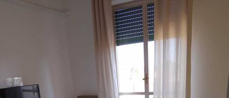 A bedroom with a bed, a TV on a dresser, and a window with curtains.