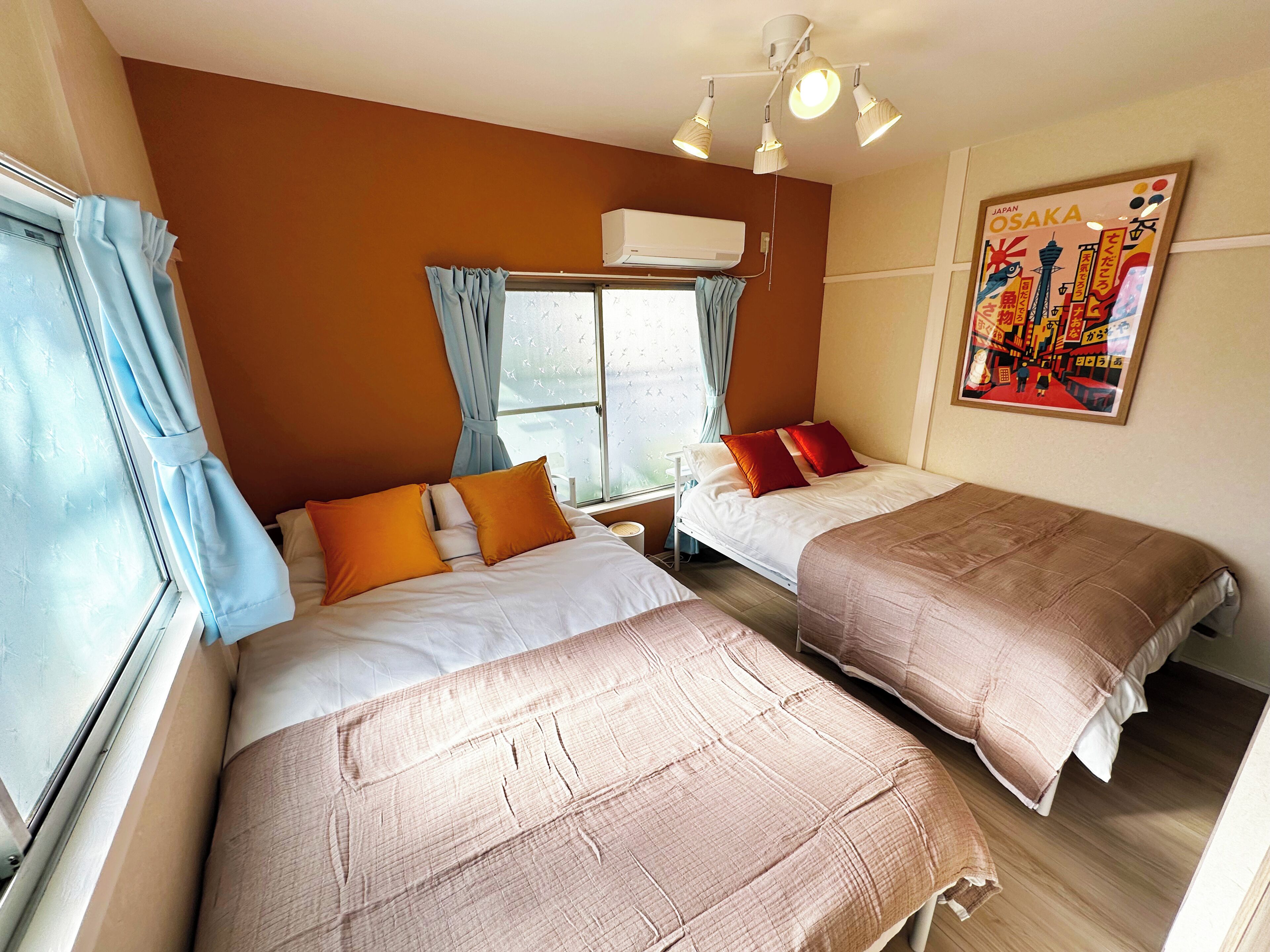 Een hotelkamer met twee bedden, een raam met gordijnen, een airconditioning en een poster aan de muur.