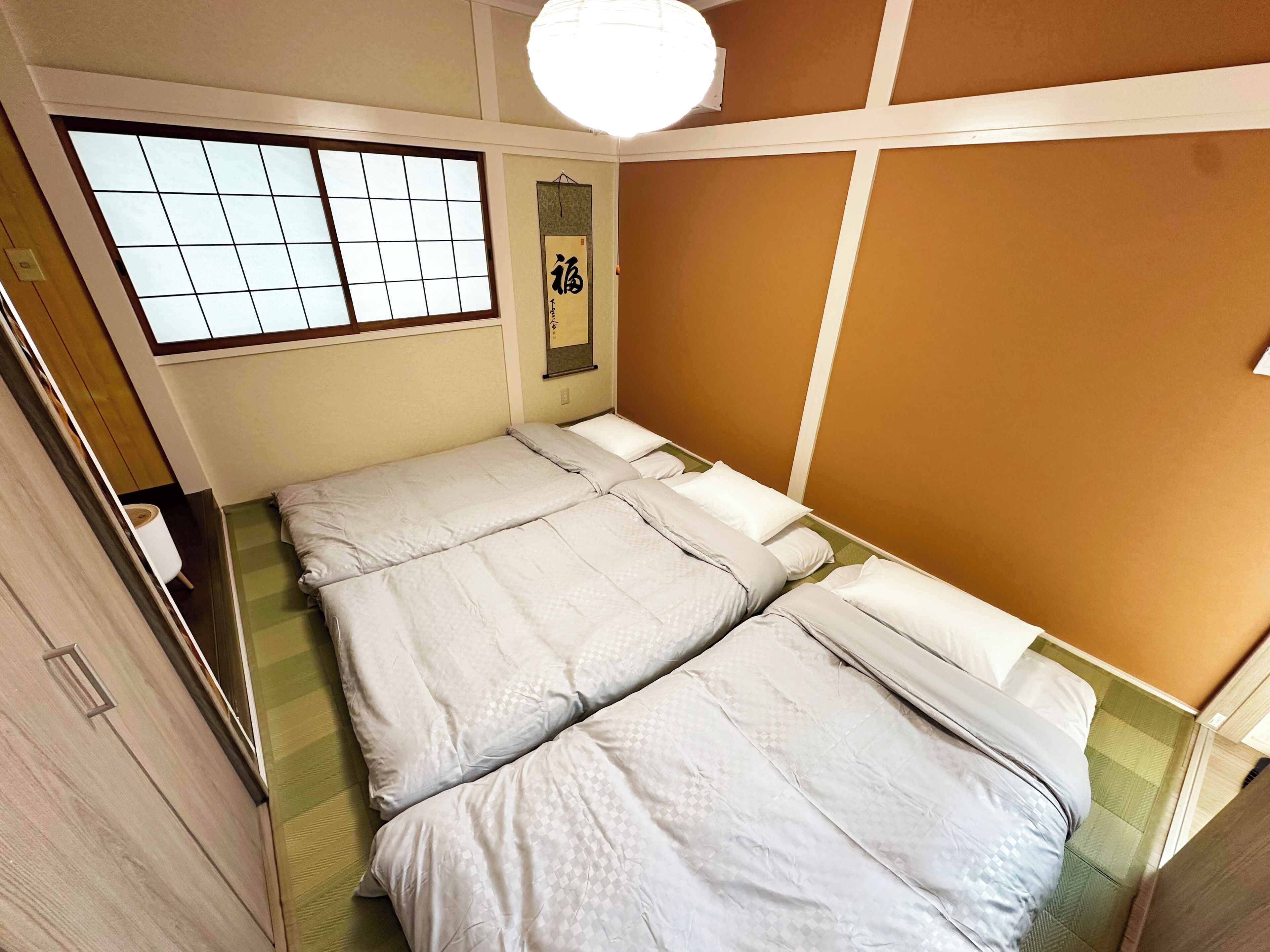 Una habitación con dos camas, una ventana con diseño de cuadrícula, un adorno colgante en la pared y una lámpara en el techo.