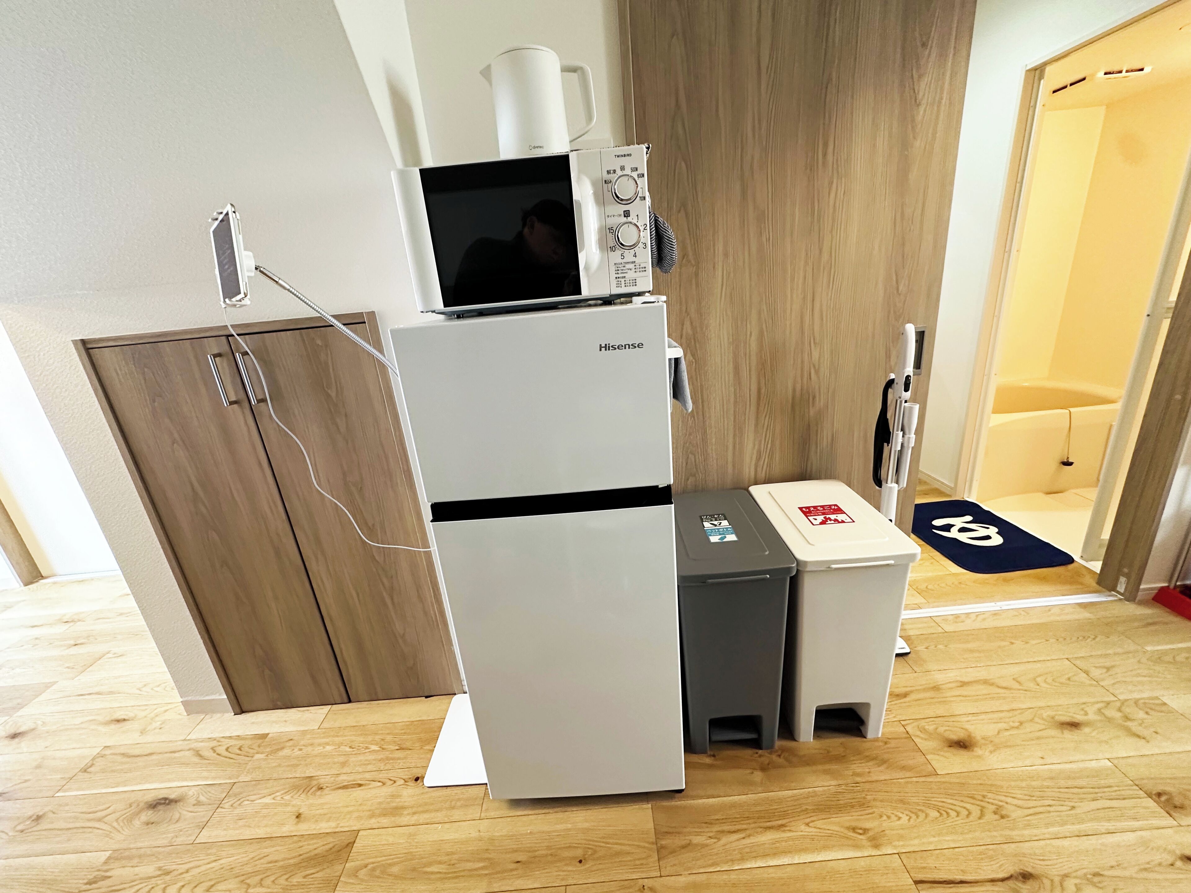 A compact kitchenette with a refrigerator, microwave, and a small trash bin.