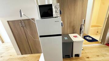 A compact kitchenette with a refrigerator, microwave, and a small trash bin.