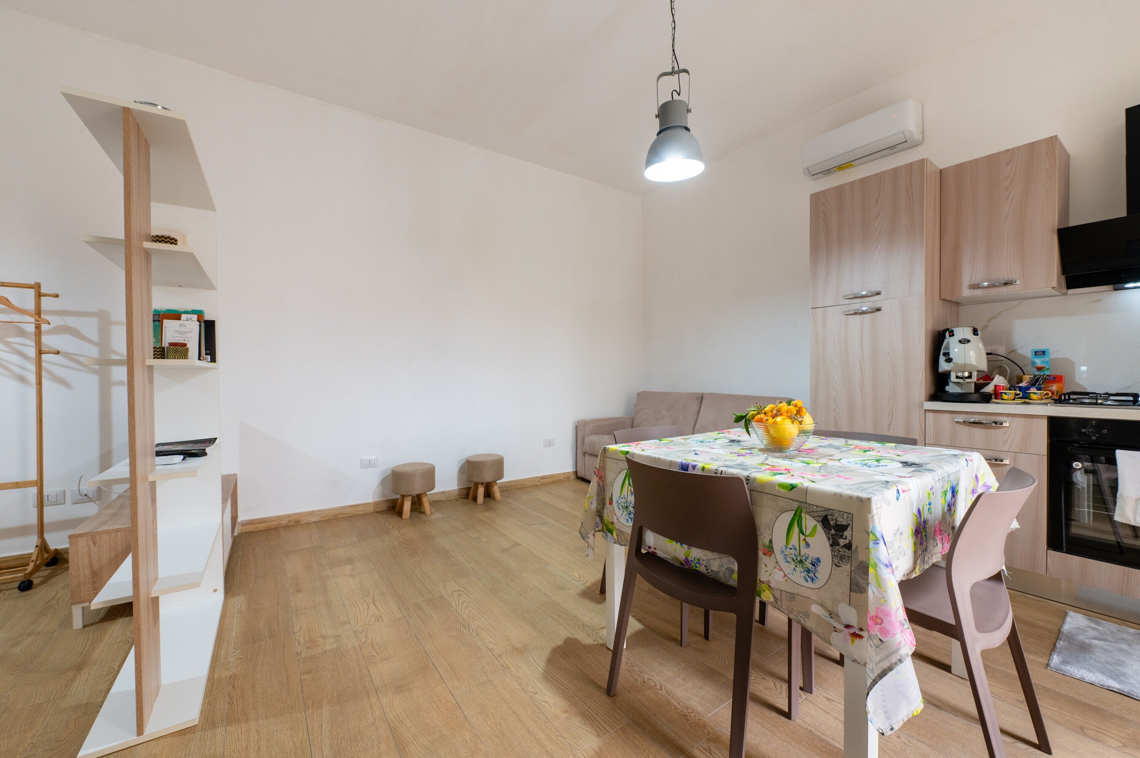 Een moderne keuken met houten kastjes, een eettafel met een tafelkleed met bloemenprint, een hanglamp en een inbouwoven.