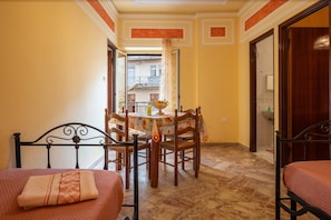Une chambre d’hôtel avec un lit, une table à manger avec des chaises, une salle de bain visible à travers une porte ouverte et un balcon avec une balustrade.