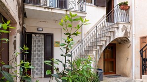 A narrow alleyway with a staircase leading to a building entrance, a potted plant in the foreground, and a door with a patterned curtain. - Family Room in Realmonte near Scala dei Turchi with Private Balcony (Realmonte)