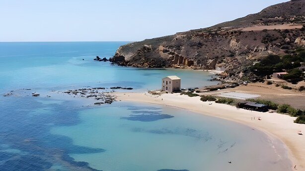 A coastal landscape with a sandy beach, clear blue waters, rocky cliffs, and a small building. - Family Room in Realmonte near Scala dei Turchi with Private Balcony (Realmonte)