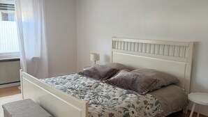 Un dormitorio con cama, mesita de noche y un taburete pequeño.