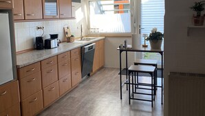 Una cocina con armarios de madera, lavavajillas, mesa y ventana con cortinas.