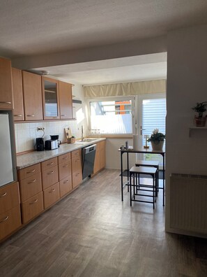 A kitchen with wooden cabinets, a dishwasher, a table, and a window with curtains.