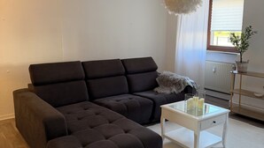 Una sala de estar con un sofá oscuro, una mesa de centro blanca y una ventana con una planta.