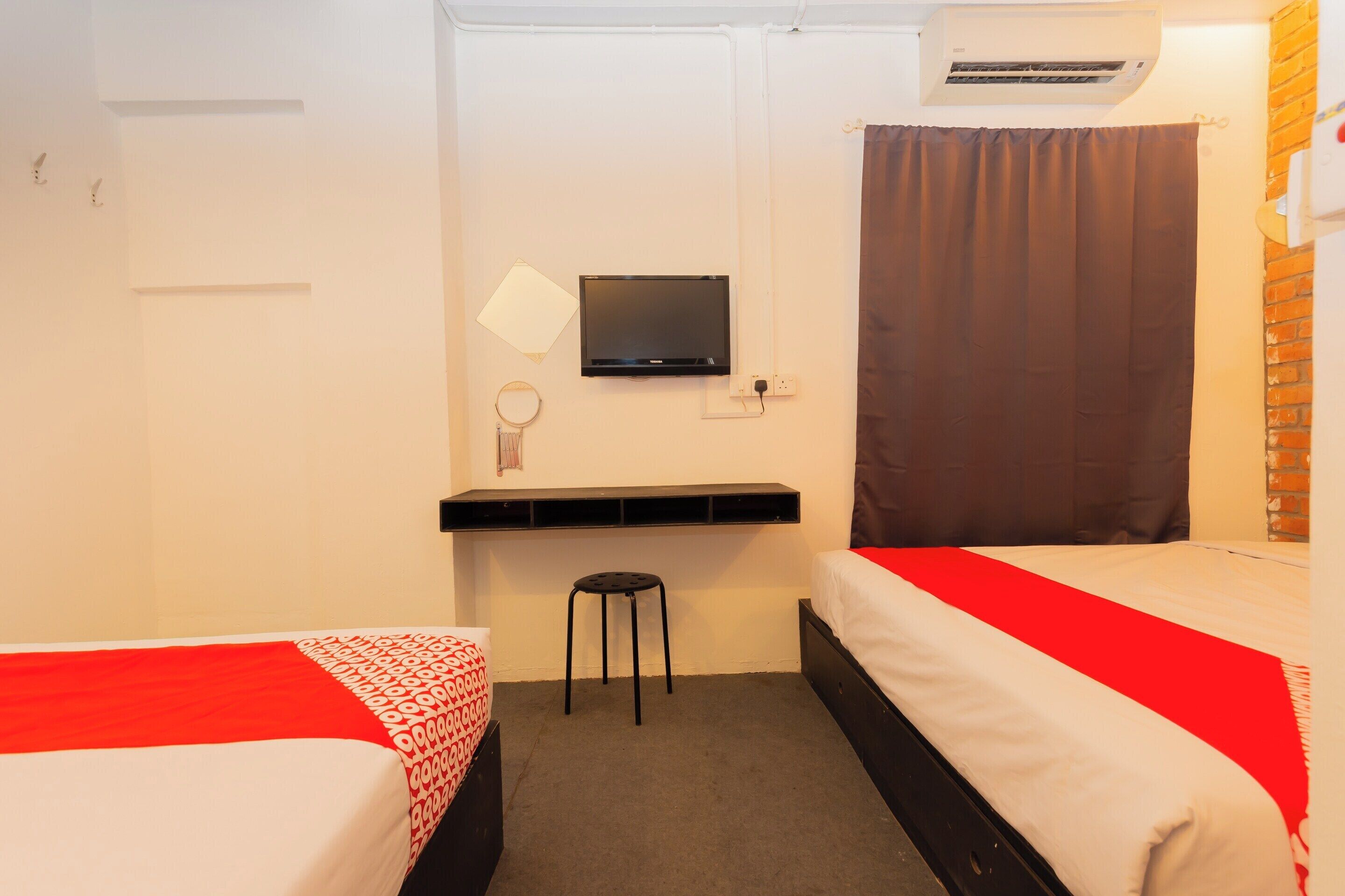 Quarto de hotel com duas camas, televisão, escrivaninha e ar condicionado.