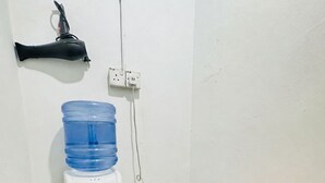 Ett litet rum med en vattenautomat, ett eluttag, ett rött strykjärn och en färgglad strykbräda.