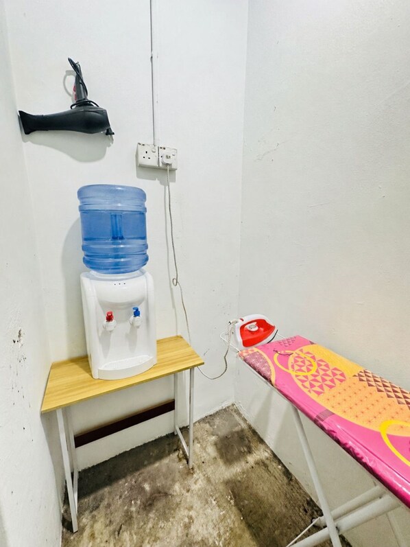 A small room with a water dispenser, a power outlet, a red iron, and a colorful ironing board. - Hotel Six Seven NearTamingSari ZZZ hotel (Malacca City)