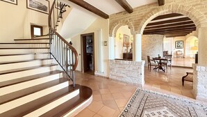 A spacious interior with a wooden staircase, stone arches, and a dining area.