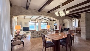 A spacious dining area with a wooden table and chairs, a chandelier, and a view through an arched doorway.
