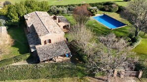 A large house with a swimming pool, surrounded by green fields and trees.