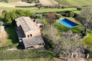 Una casa grande con piscina, rodeada de campos verdes y árboles.