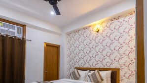 A bedroom with a bed, a desk, a chair, a ceiling fan, and a wall-mounted light fixture. - The Empire Sector 45 Gurgaon (Gurugram)