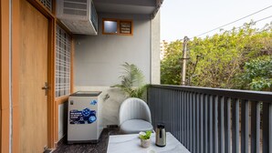 A balcony with a washing machine, a chair, a small table with a plant, and a water dispenser. - The Empire Sector 45 Gurgaon (Gurugram)